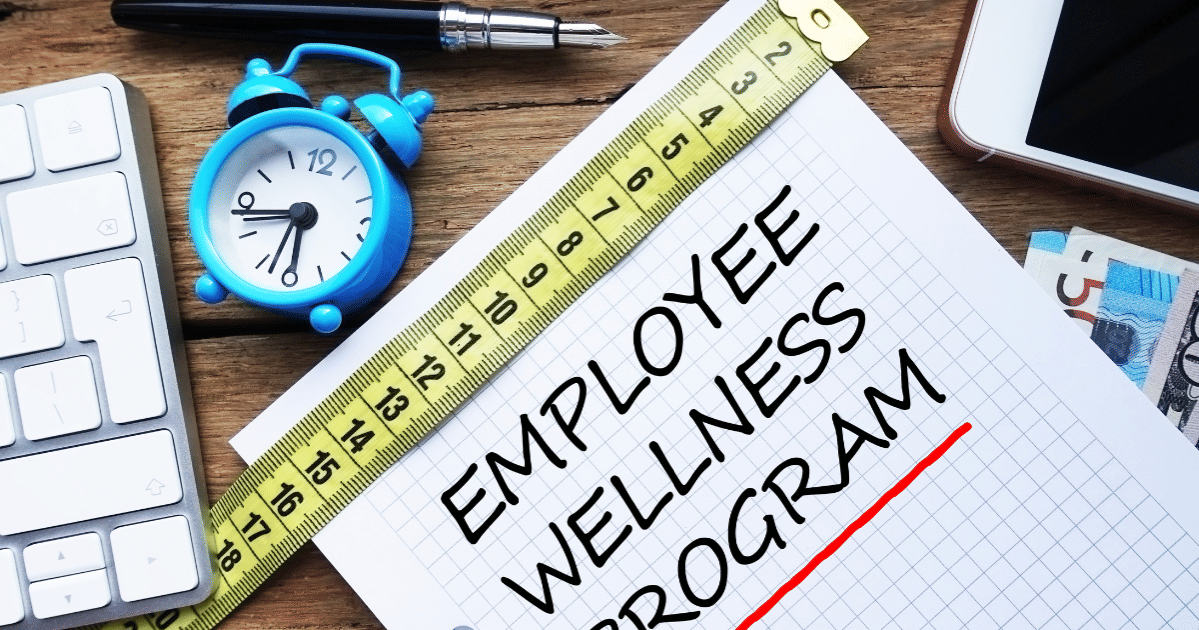 Cluttered office desk with notepad containing employee wellness program written on it